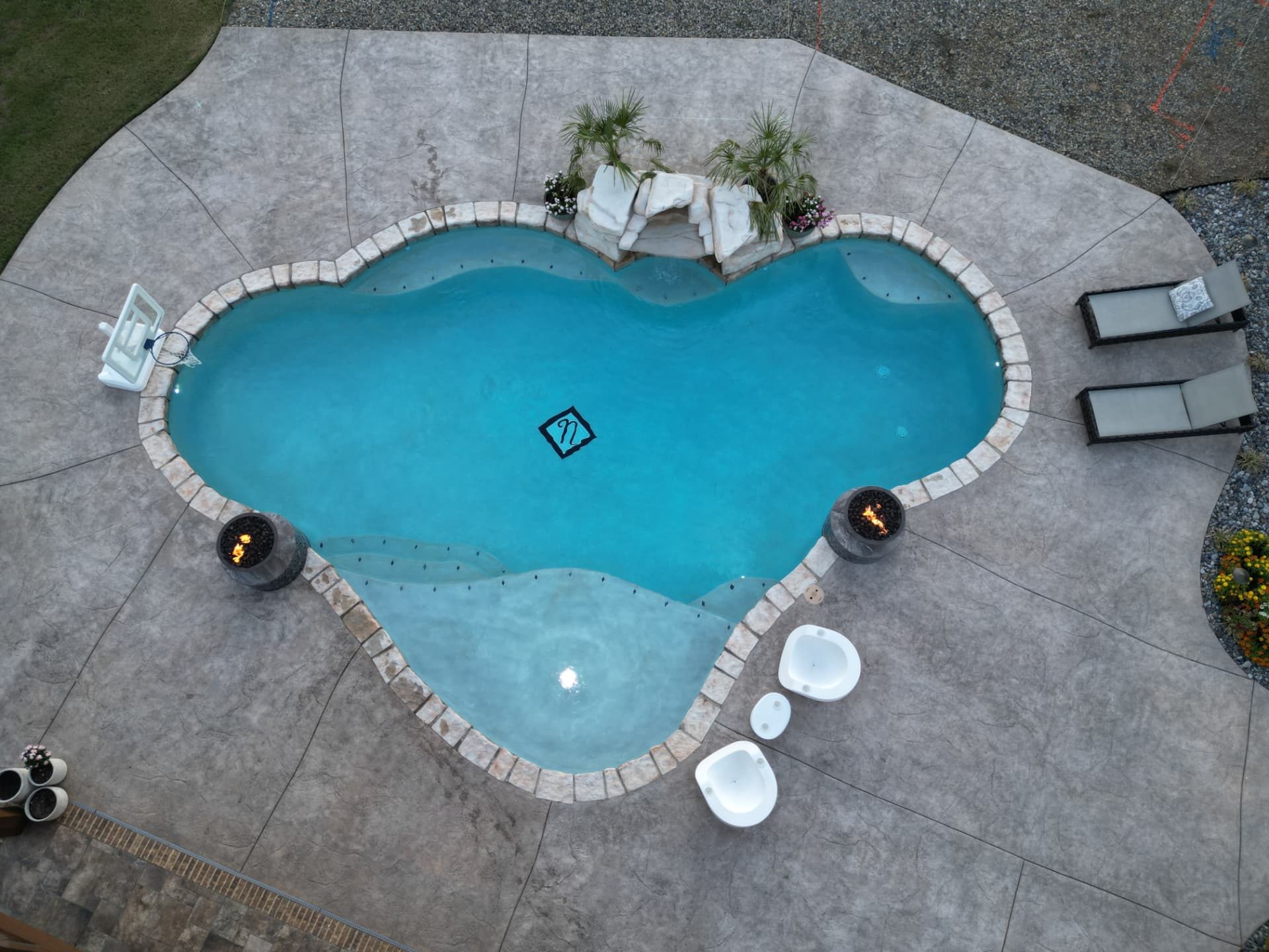 Custom pool with fire bowls on pillars and a waterfall spilling into the deep end