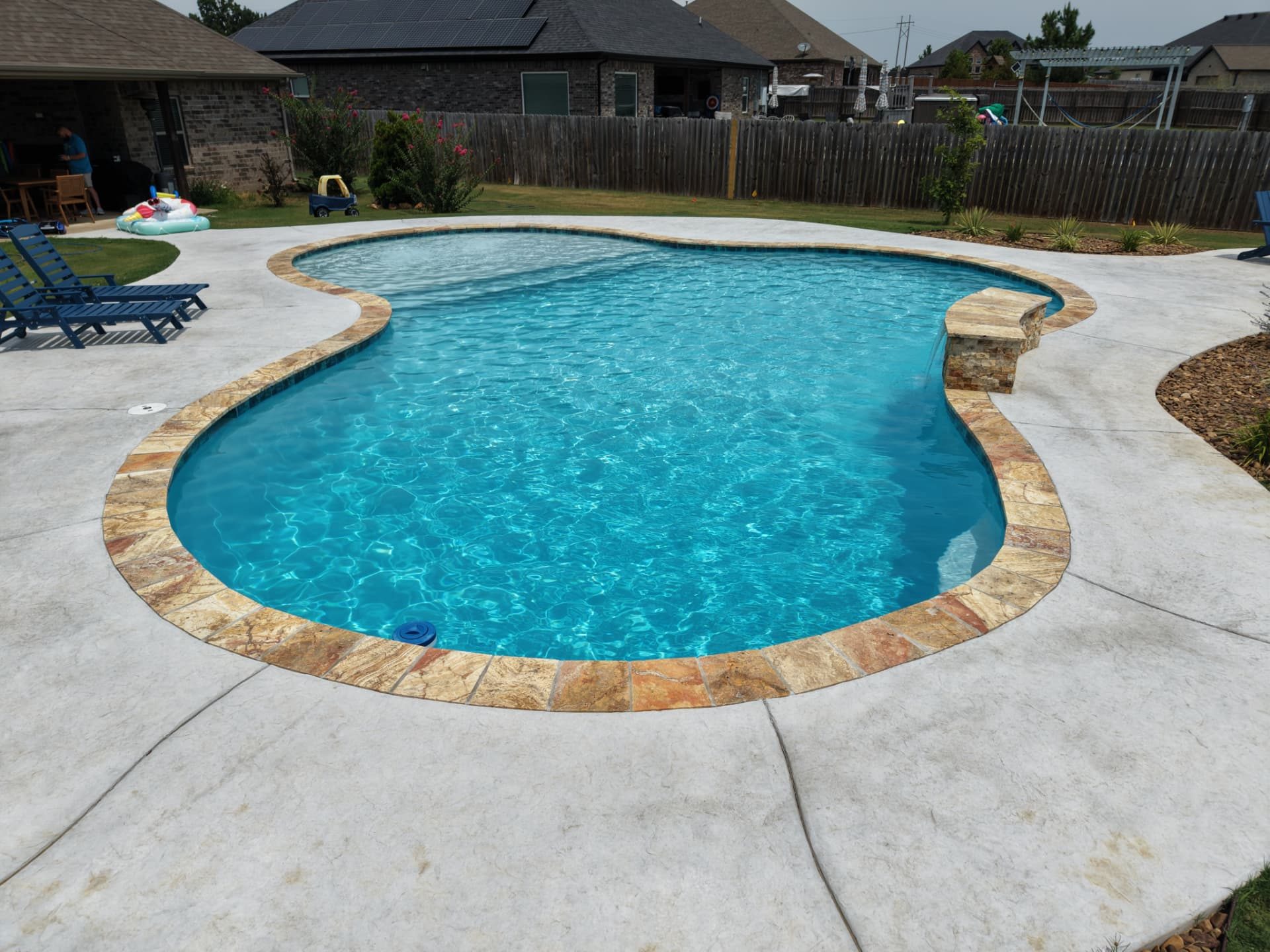 Freeform gunite pool with tan coping and a small stone waterfall