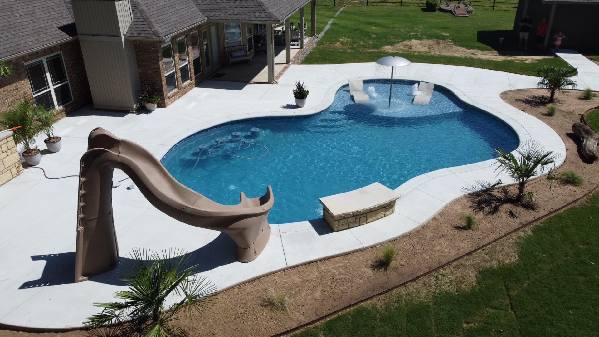 Freeform gunite pool with a built-in umbrella, loungers in the shallow water, and a slide